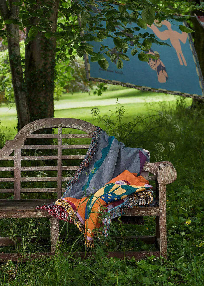 A colourful throw blanket featuring an illustration of a bird, an ostrich, and a jackal in a whimsical morning scene with the text 'Good morning' at the bottom,  available  to buy on the-salon.com. SALON curates the finest , unique, handmade pieces from the interior industry's best makers and brands. Shop luxury furniture, lighting, rugs, art, antiques and vintage pieces and accessories from SALON interior designed rooms.