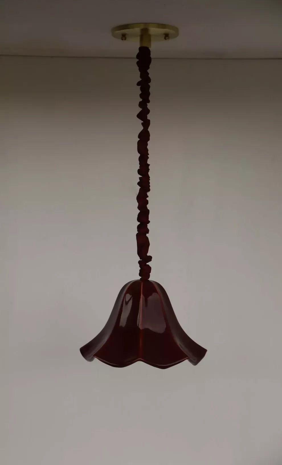 A red, conical pendant light with a glossy finish and a silk satin cord cover,  available  to buy on the-salon.com. SALON curates the finest , unique, handmade pieces from the interior industry's best makers and brands. Shop luxury furniture, lighting, rugs, art, antiques and vintage pieces and accessories from SALON interior designed rooms.