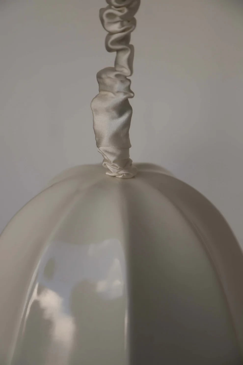 A close up of the silk satin cord cover on a white, conical pendant light with a glossy finish and a silk satin cord cover,  available  to buy on the-salon.com. SALON curates the finest , unique, handmade pieces from the interior industry's best makers and brands. Shop luxury furniture, lighting, rugs, art, antiques and vintage pieces and accessories from SALON interior designed rooms.