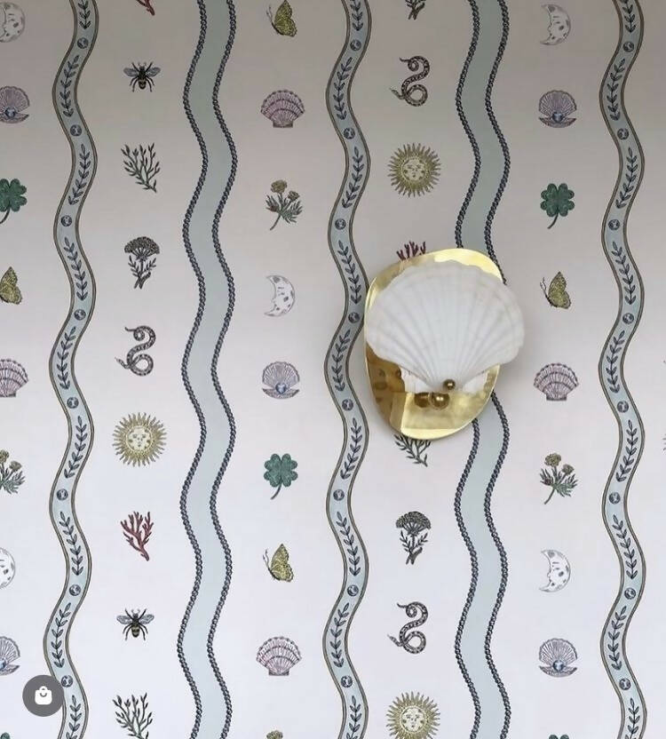 A wall light fixture with a chalky white scallop shell finish mounted on a polished brass backplate,  available  to buy on the-salon.com. SALON curates the finest , unique, handmade pieces from the interior industry's best makers and brands. Shop luxury furniture, lighting, rugs, art, antiques and vintage pieces and accessories from SALON interior designed rooms.