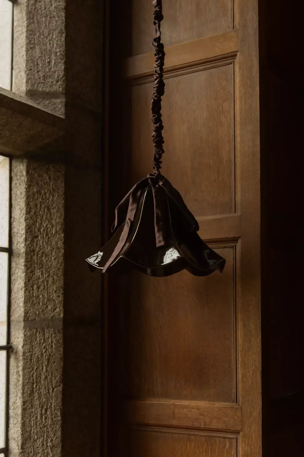 A brown, conical pendant light with a glossy finish and a silk satin cord cover,  available  to buy on the-salon.com. SALON curates the finest , unique, handmade pieces from the interior industry's best makers and brands. Shop luxury furniture, lighting, rugs, art, antiques and vintage pieces and accessories from SALON interior designed rooms.