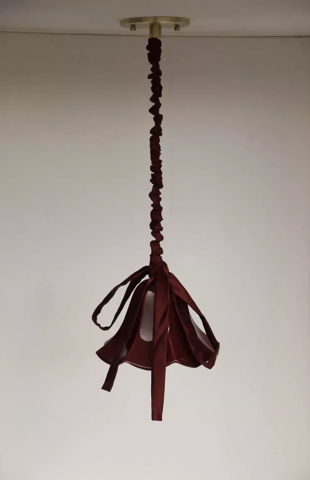 A red, conical pendant light with a glossy finish and a silk satin cord cover,  available  to buy on the-salon.com. SALON curates the finest , unique, handmade pieces from the interior industry's best makers and brands. Shop luxury furniture, lighting, rugs, art, antiques and vintage pieces and accessories from SALON interior designed rooms.