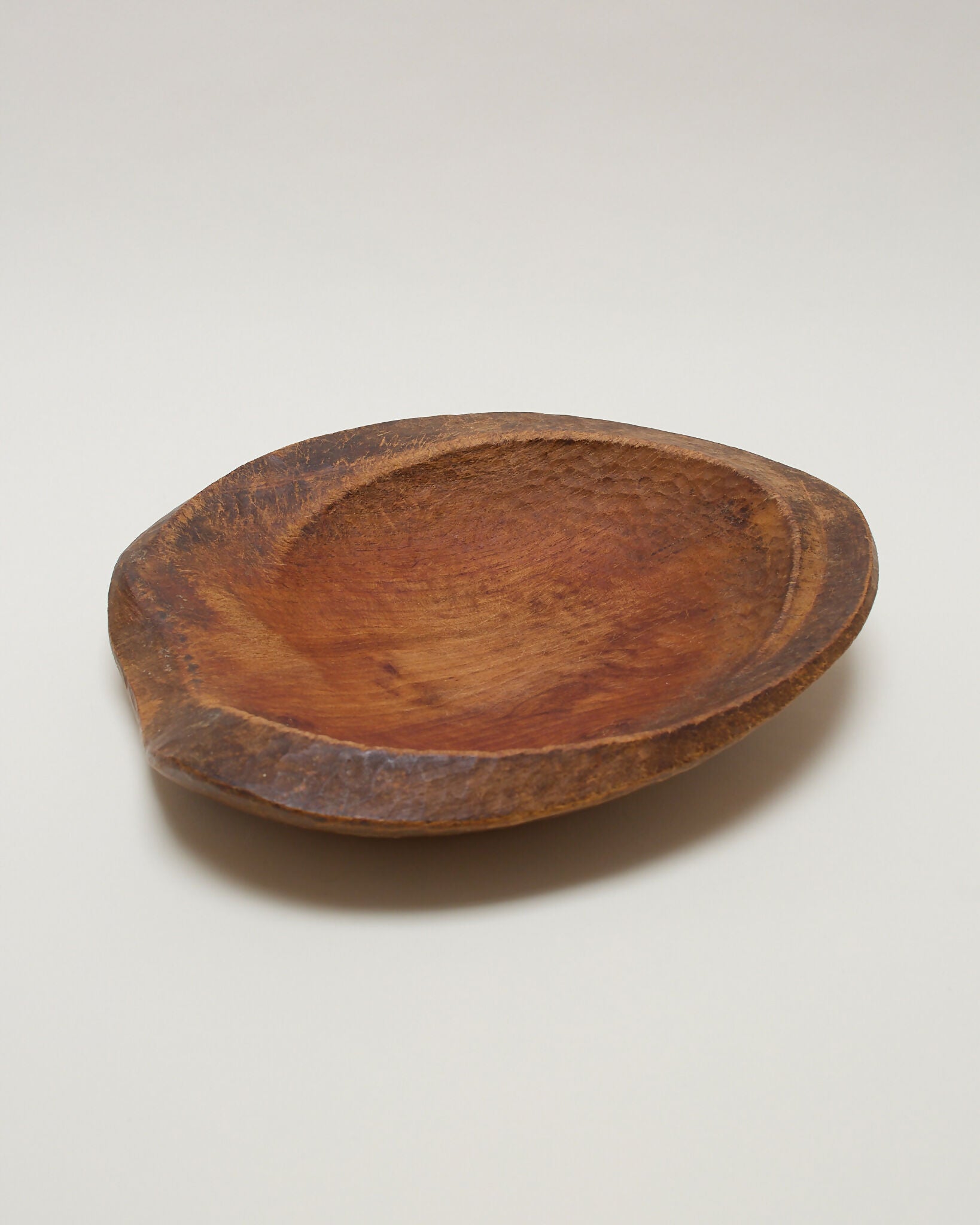 A hand-carved wooden bowl with a natural finish, displaying visible signs of craftsmanship,  available  to buy on the-salon.com. SALON curates the finest , unique, handmade pieces from the interior industry's best makers and brands. Shop luxury furniture, lighting, rugs, art, antiques and vintage pieces and accessories from SALON interior designed rooms.
