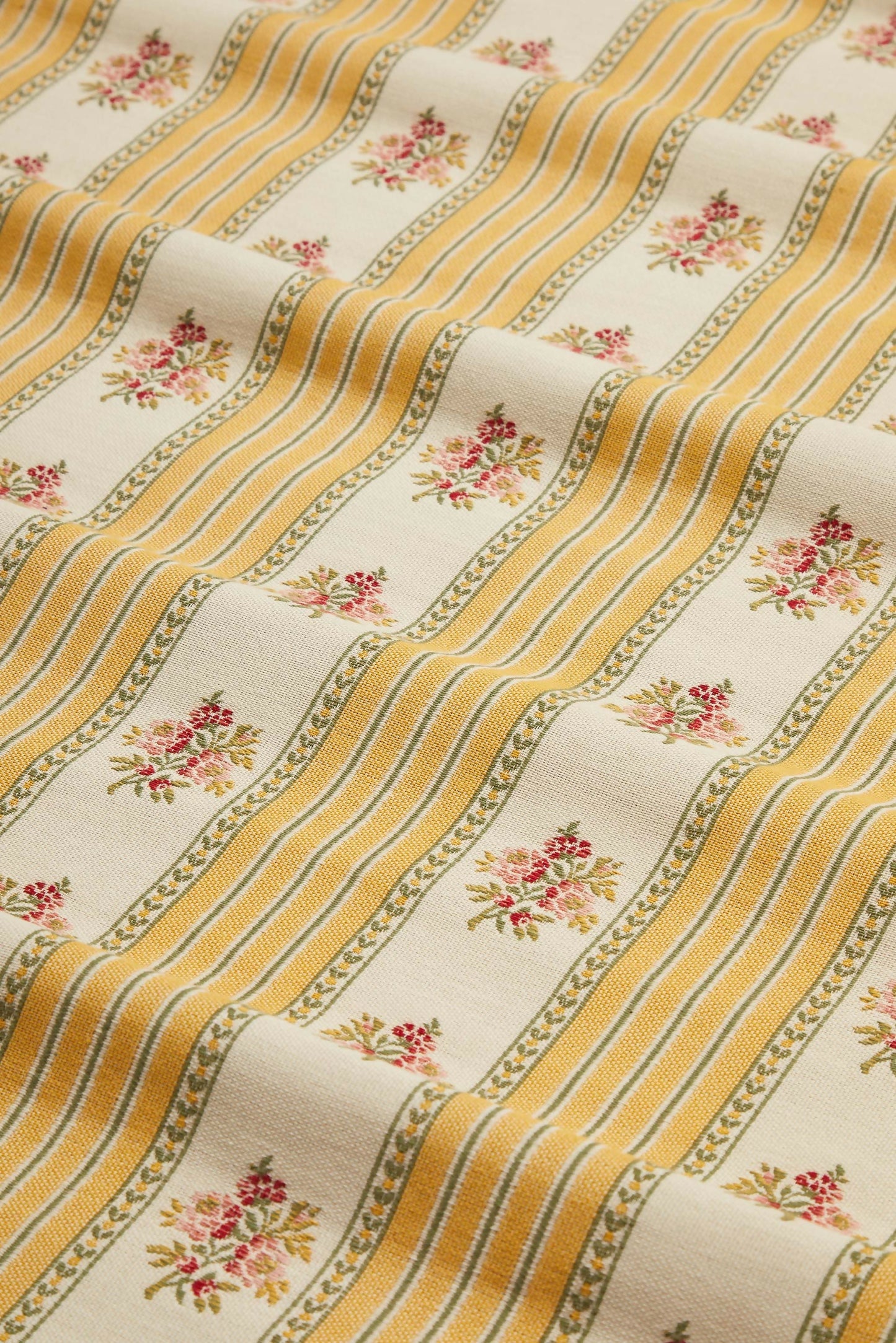 Close-up view of a jacquard weave fabric featuring a sofa stripe pattern with yellow and green stripes and embroidered floral motifs,  available  to buy on the-salon.com. SALON curates the finest , unique, handmade pieces from the interior industry's best makers and brands. Shop luxury furniture, lighting, rugs, art, antiques and vintage pieces and accessories from SALON interior designed rooms.