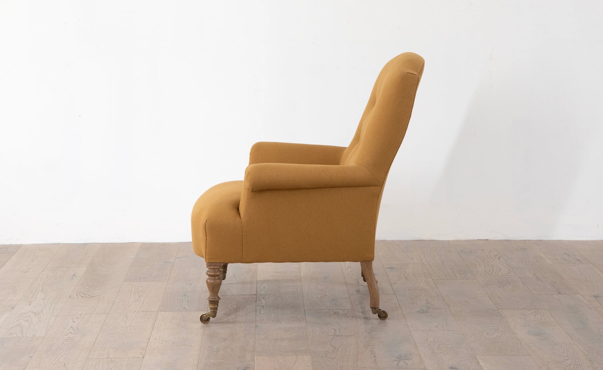 A brown upholstered armchair with button back detailing and scroll arms, set against a white background,  available  to buy on the-salon.com. SALON curates the finest , unique, handmade pieces from the interior industry's best makers and brands. Shop luxury furniture, lighting, rugs, art, antiques and vintage pieces and accessories from SALON interior designed rooms.