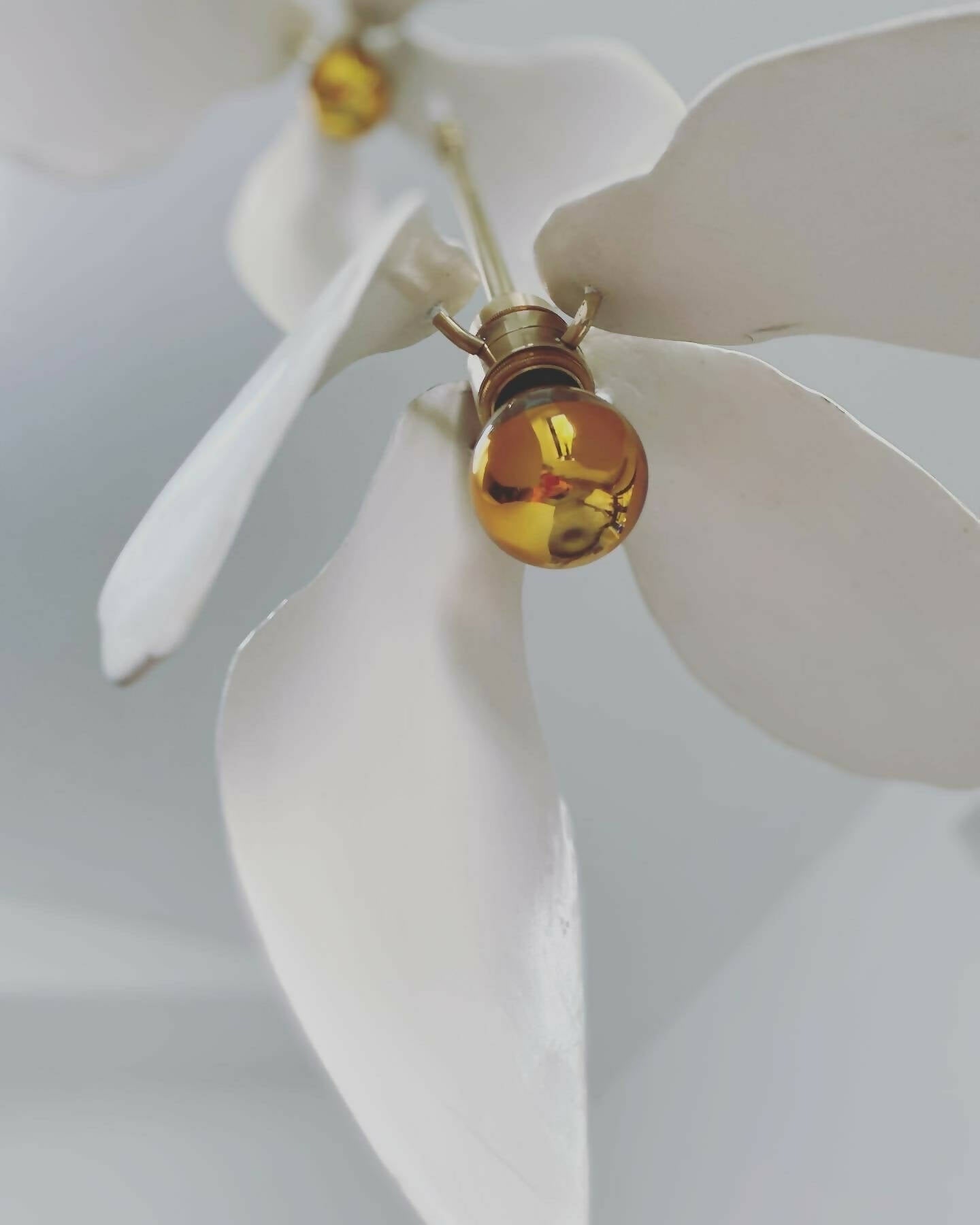 A close-up image of a white magnolia flower pendant light with a brass fitting and a gold-topped SES lamp,  available  to buy on the-salon.com. SALON curates the finest , unique, handmade pieces from the interior industry's best makers and brands. Shop luxury furniture, lighting, rugs, art, antiques and vintage pieces and accessories from SALON interior designed rooms.
