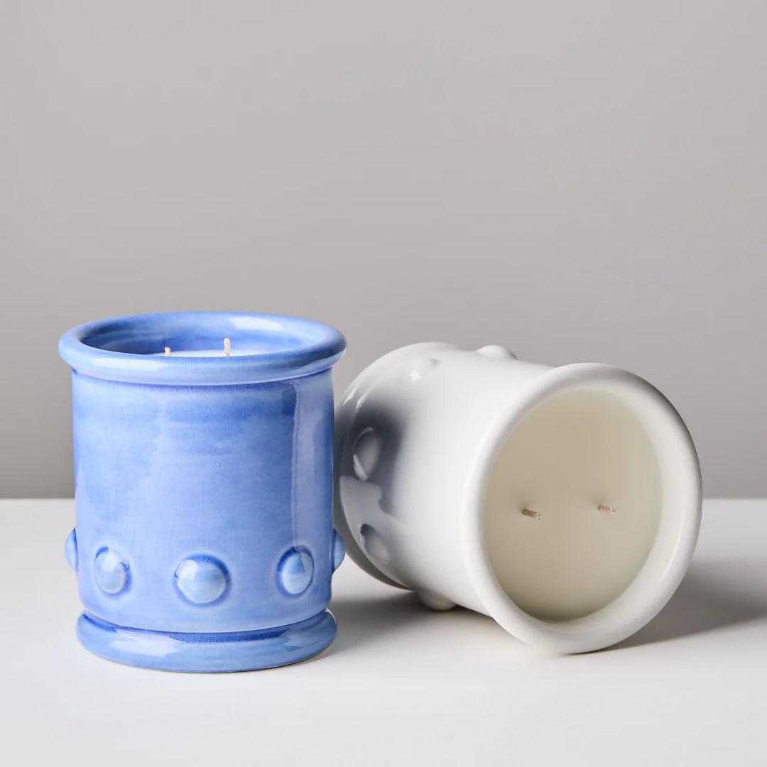 Blue and white ceramic candle vessels with spherical detailing on the sides, with a candle visible at the top. The vessel is placed against a neutral background,  available  to buy on the-salon.com. SALON curates the finest , unique, handmade pieces from the interior industry's best makers and brands. Shop luxury furniture, lighting, rugs, art, antiques and vintage pieces and accessories from SALON interior designed rooms.