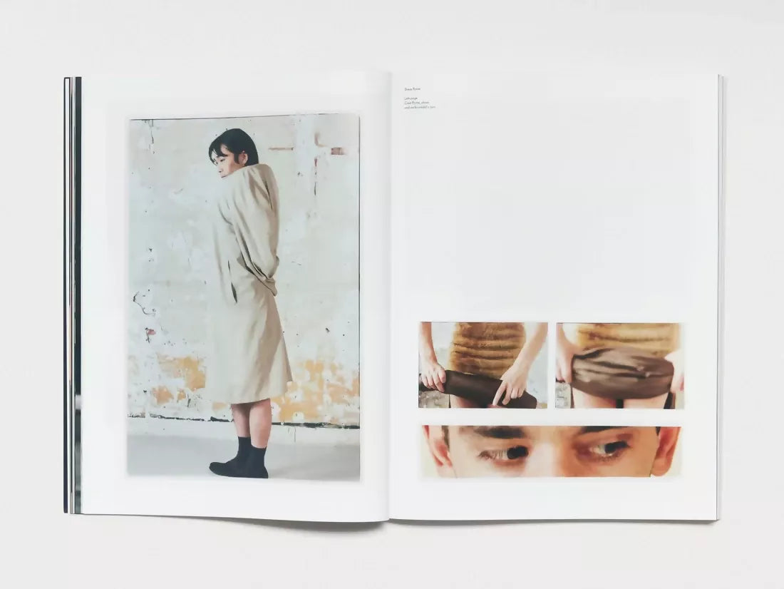 An open book, pages to three pages, one being a woman stood up in black socks next to a dirty wall and wearing a large trench coat, the other two being a photo of eyes looking to the side and the last being a piece of brown fabric being rolled up, available  to buy on the-salon.com. SALON curates the finest , unique, handmade pieces from the interior industry's best makers and brands. Shop luxury furniture, lighting, rugs, art, antiques and vintage pieces and accessories from SALON interior designed rooms.