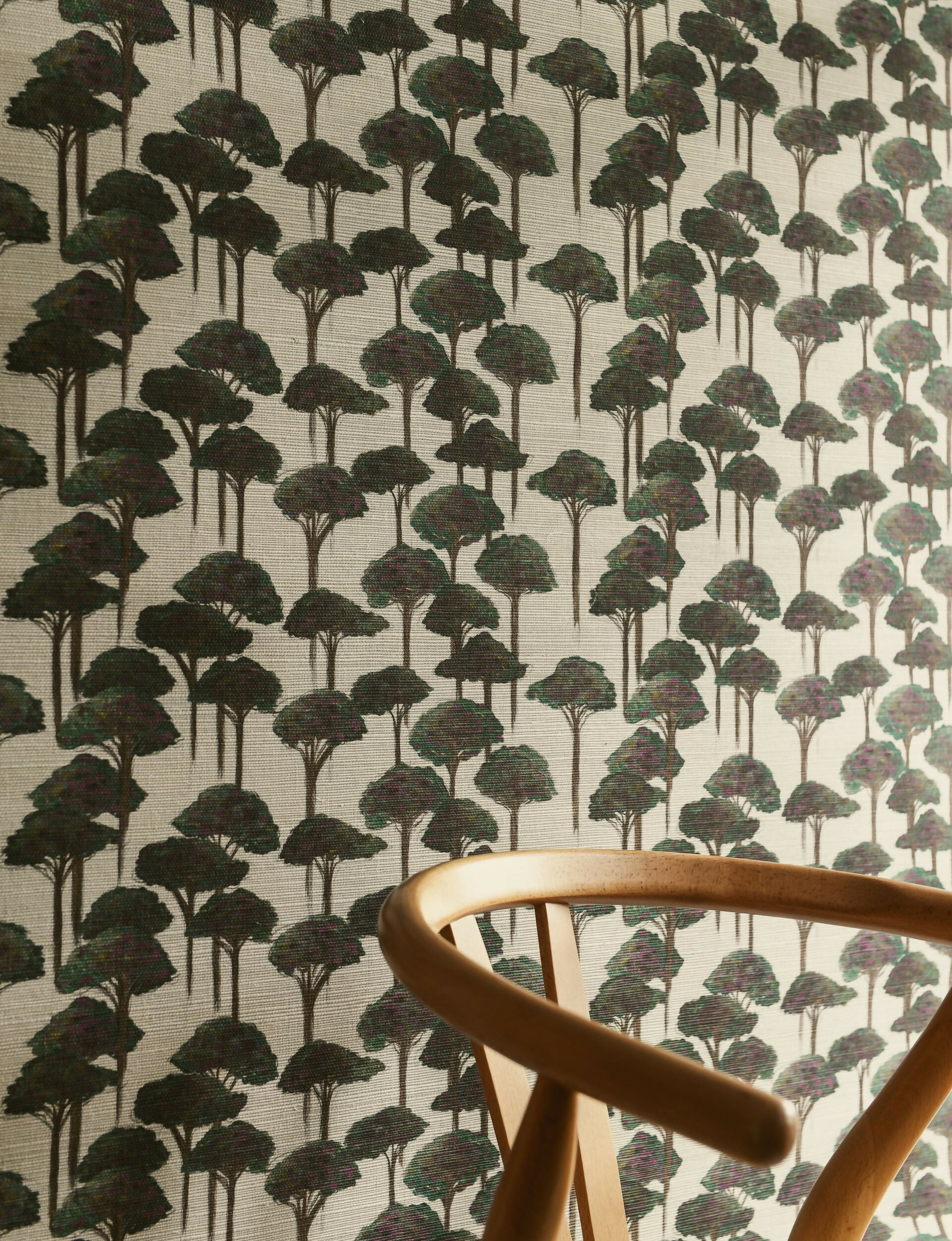 A room with wallpaper featuring a pattern of stylized pine trees and umbrellas in green shades, with two cushions in the foreground, available  to buy on the-salon.com. SALON curates the finest , unique, handmade pieces from the interior industry's best makers and brands. Shop luxury furniture, lighting, rugs, art, antiques and vintage pieces and accessories from SALON interior designed rooms.