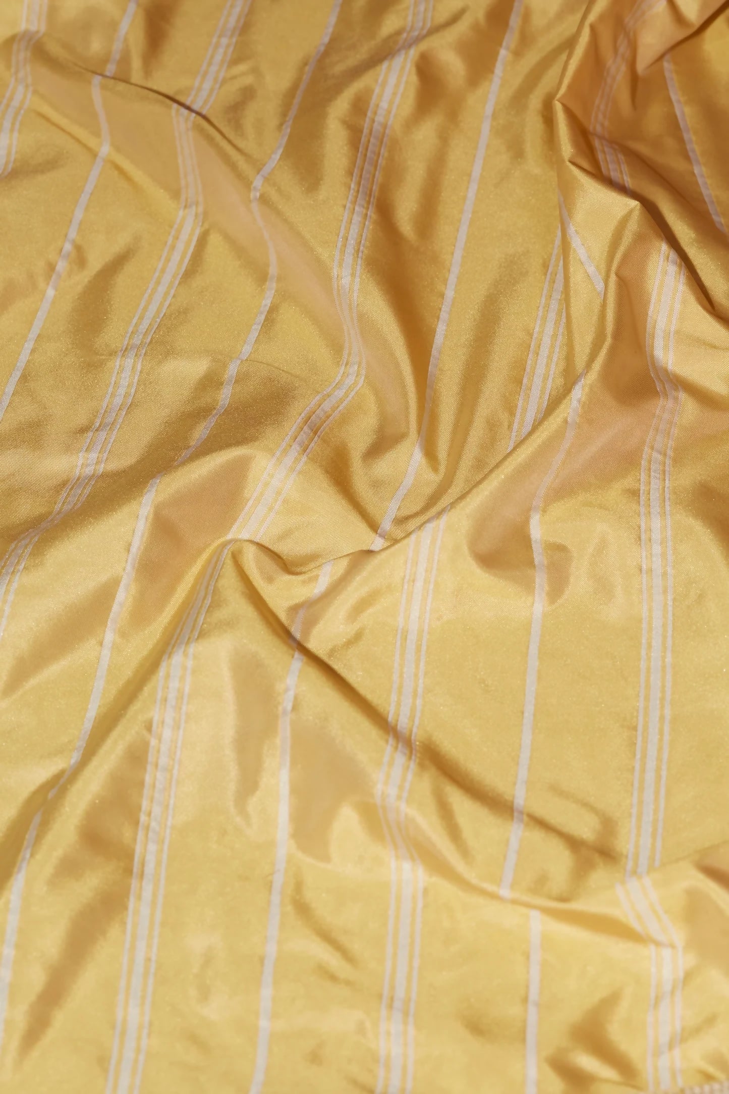 A close-up image of a yellow taffeta stripe fabric with a pin stripe pattern,  available  to buy on the-salon.com. SALON curates the finest , unique, handmade pieces from the interior industry's best makers and brands. Shop luxury furniture, lighting, rugs, art, antiques and vintage pieces and accessories from SALON interior designed rooms.
