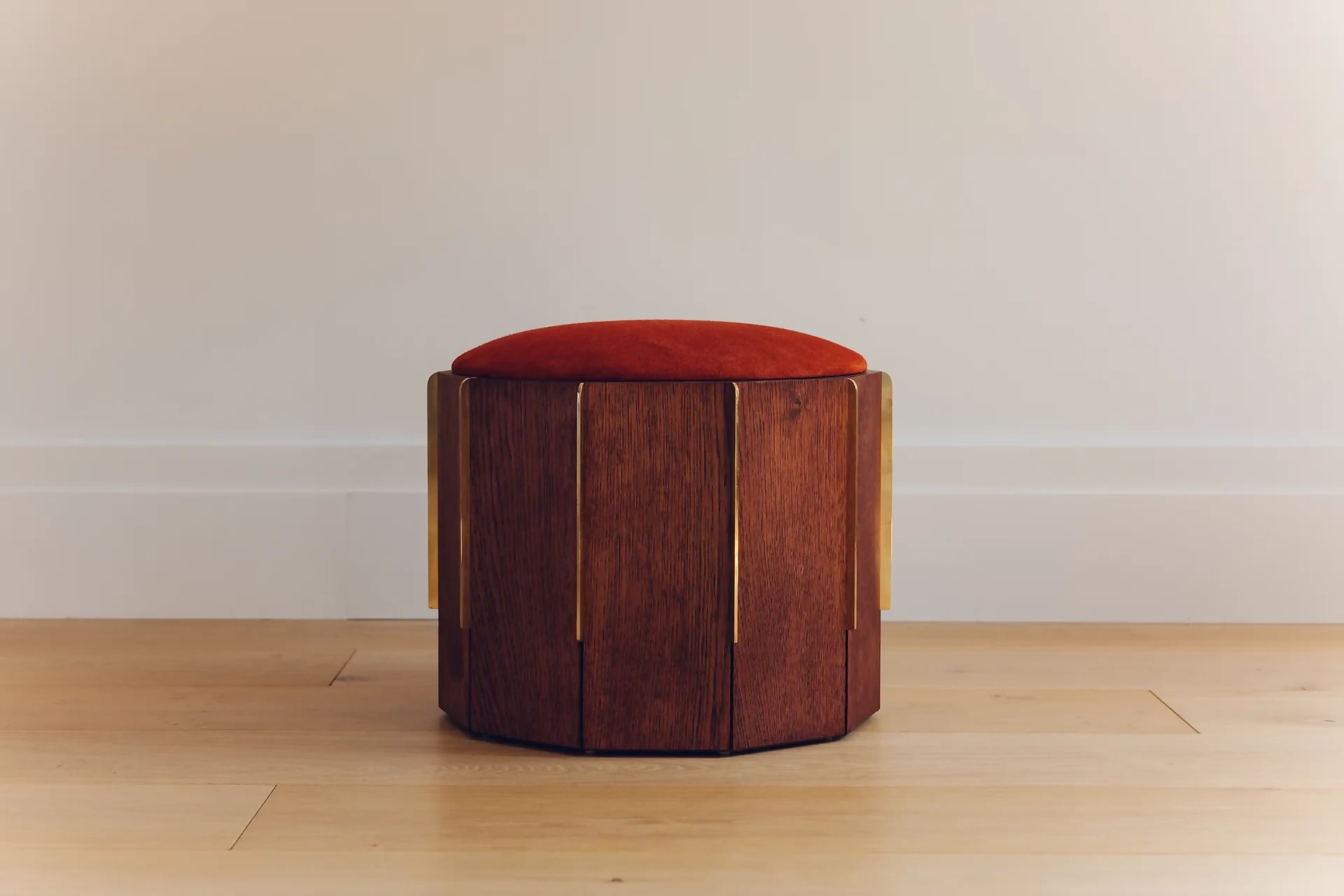 Wooden stool with a red cushion on a wooden floor against a white wall