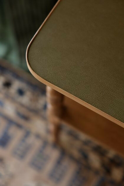 A close up of the brown wooden bedside table with a leather top, placed on a patterned carpet,  available  to buy on the-salon.com. SALON curates the finest , unique, handmade pieces from the interior industry's best makers and brands. Shop luxury furniture, lighting, rugs, art, antiques and vintage pieces and accessories from SALON interior designed rooms.