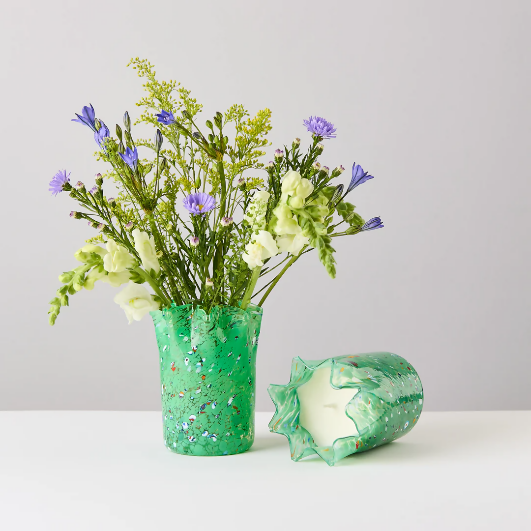 A custom hand-blown green glass candle holder with embedded colorful glass pieces, displayed alongside its lid, on a white surface,  available  to buy on the-salon.com. SALON curates the finest , unique, handmade pieces from the interior industry's best makers and brands. Shop luxury furniture, lighting, rugs, art, antiques and vintage pieces and accessories from SALON interior designed rooms.