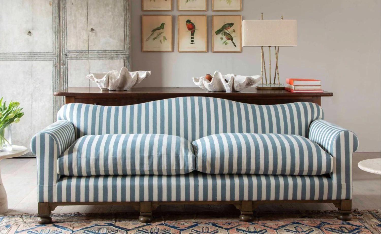 A blue and white striped camel back sofa with solid oak turned legs in a room with decorative items on top, available  to buy on the-salon.com. SALON curates the finest , unique, handmade pieces from the interior industry's best makers and brands. Shop luxury furniture, lighting, rugs, art, antiques and vintage pieces and accessories from SALON interior designed rooms.