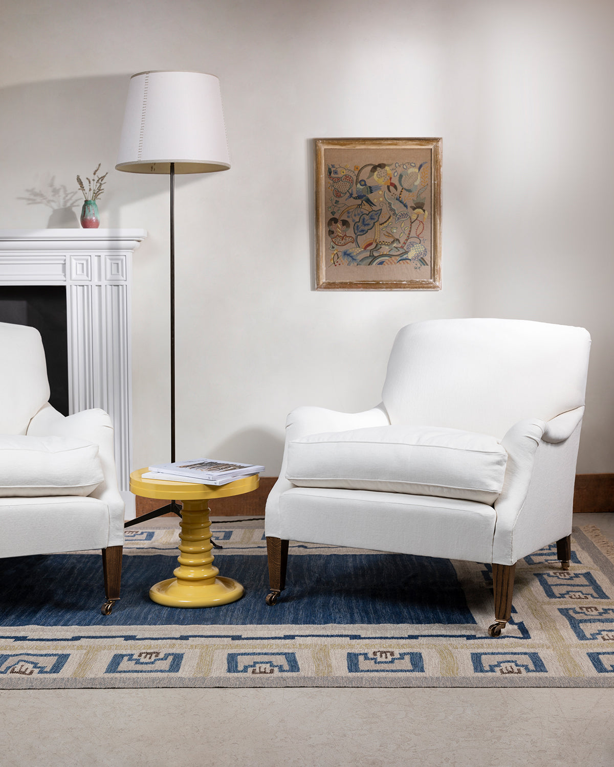 An image of a living room with two white chairs and a white lamp with the white fireplace in the background against a white wall with a blue geometrically patterned rug,  available  to buy on the-salon.com. SALON curates the finest , unique, handmade pieces from the interior industry's best makers and brands. Shop luxury furniture, lighting, rugs, art, antiques and vintage pieces and accessories from SALON interior designed rooms.