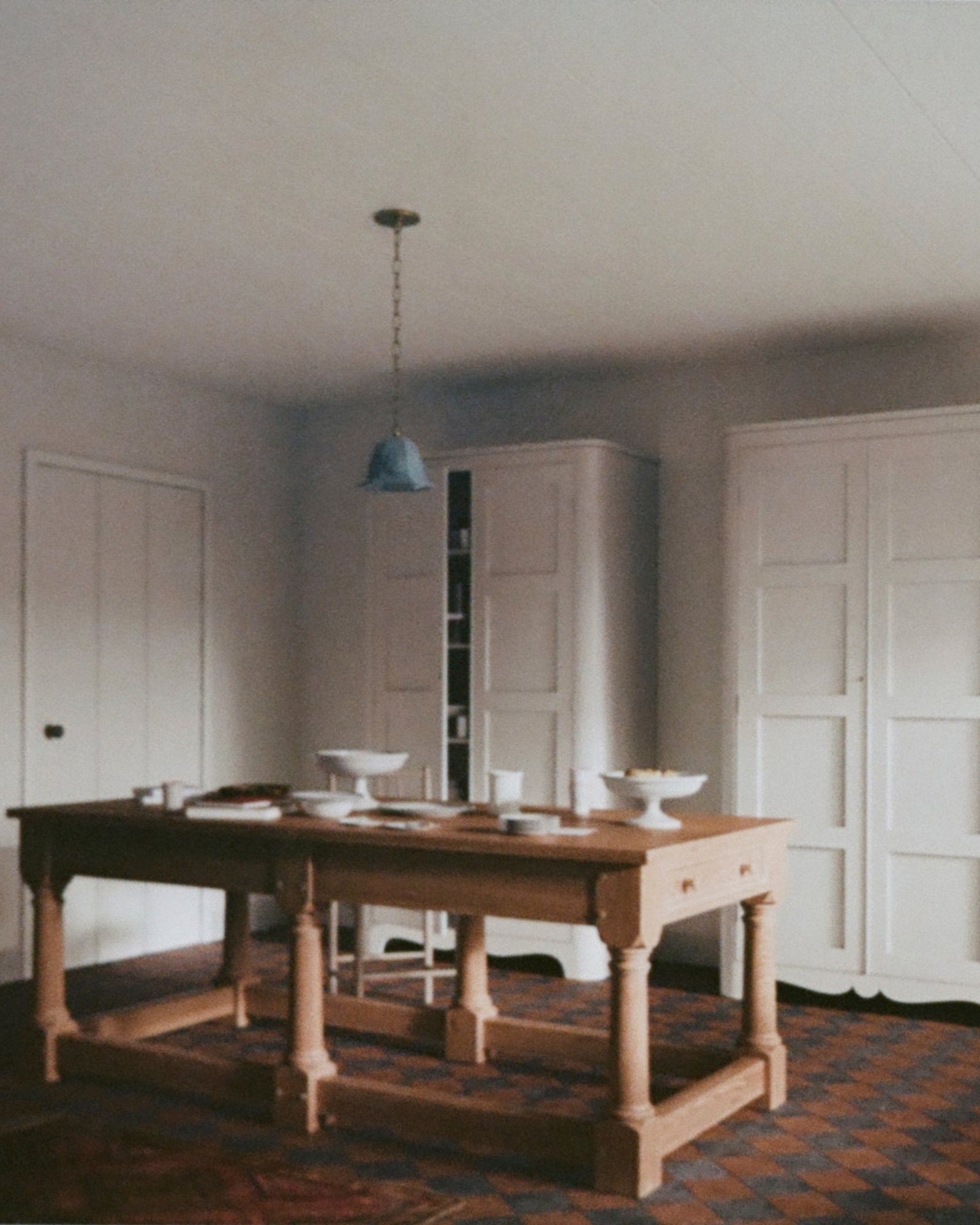 A rectangular wooden refectory table with drawers at each end, placed in a room with white walls and a patterned floor,  available  to buy on the-salon.com. SALON curates the finest , unique, handmade pieces from the interior industry's best makers and brands. Shop luxury furniture, lighting, rugs, art, antiques and vintage pieces and accessories from SALON interior designed rooms.