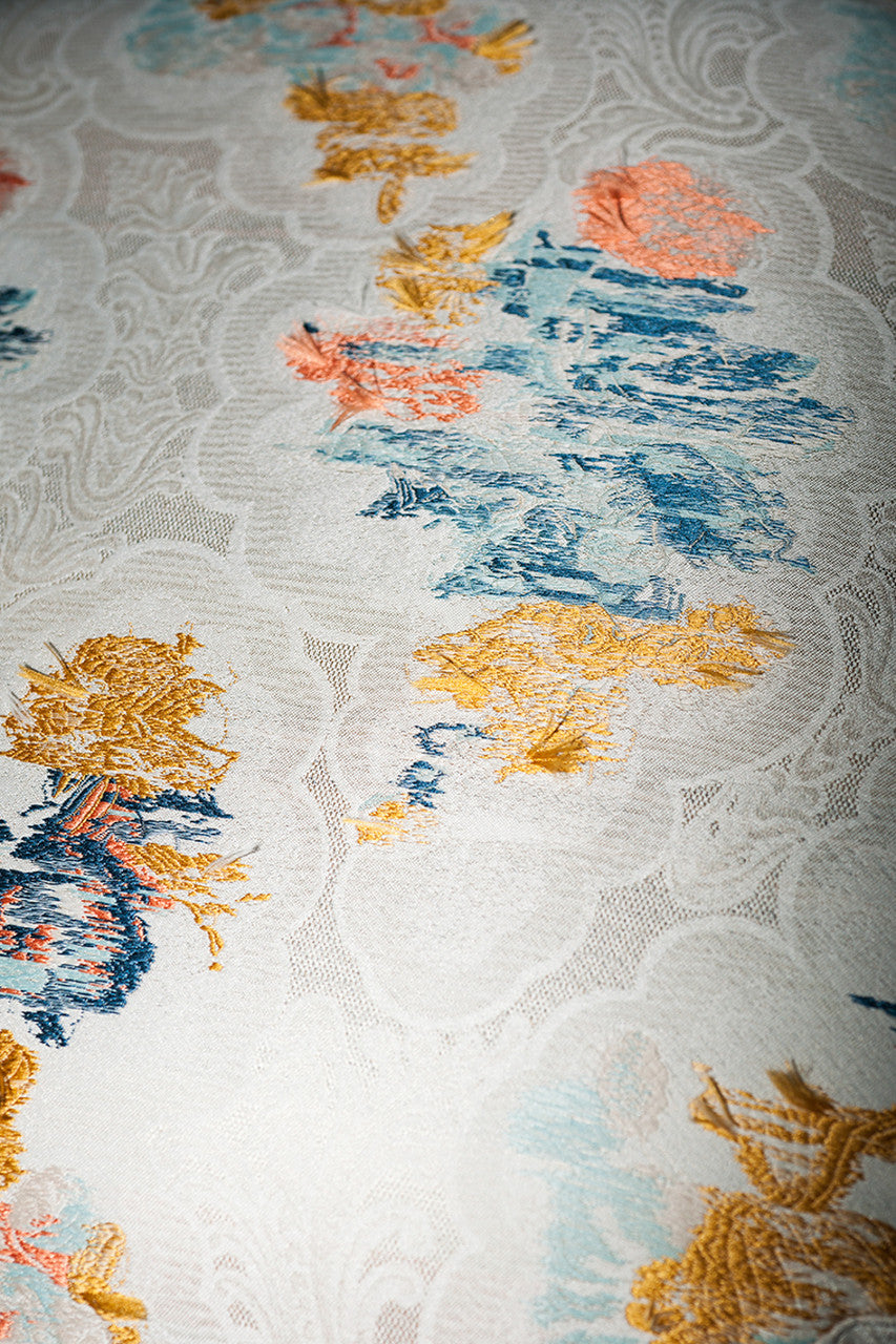 An image of a piece of fabric with yellow, blue and pink colours on a white lace background, available  to buy on the-salon.com. SALON curates the finest , unique, handmade pieces from the interior industry's best makers and brands. Shop luxury furniture, lighting, rugs, art, antiques and vintage pieces and accessories from SALON interior designed rooms.
