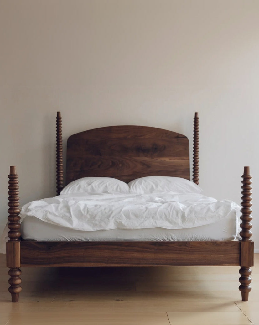 Wooden bed with white bedding against a plain wall
