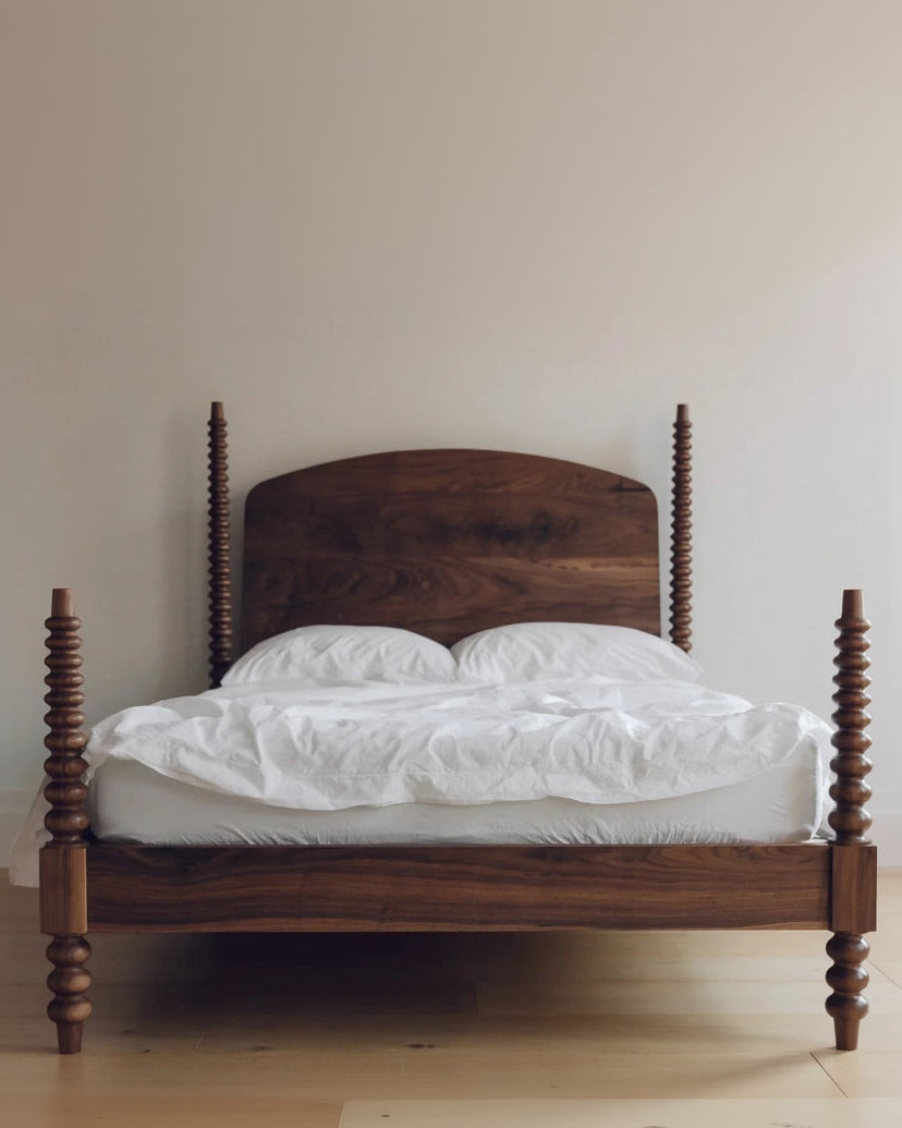 Wooden bed with white bedding against a plain wall