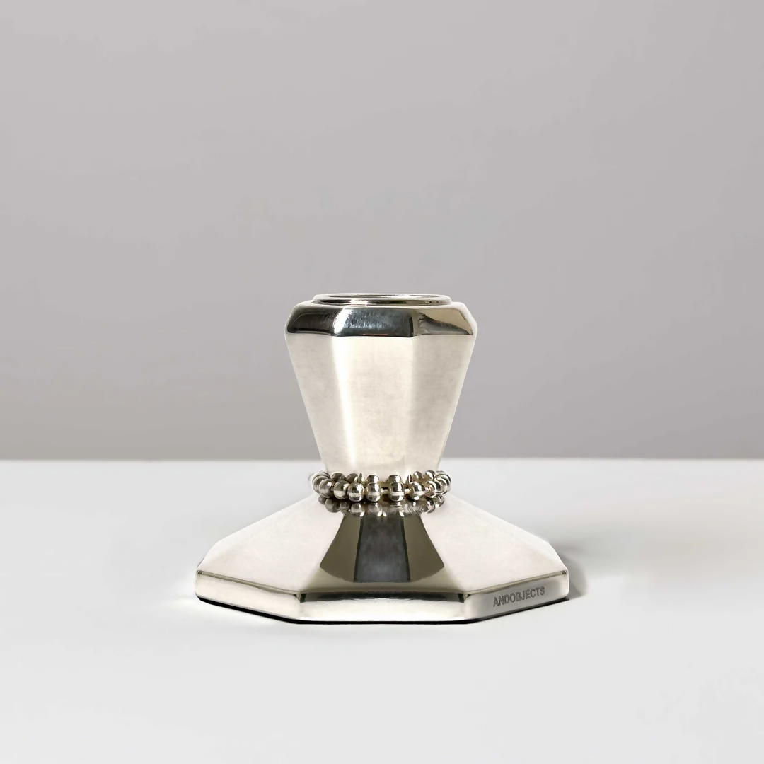 A silver candle stick on a white background, featuring intricate beaded detailing around the neck and an angular base,  available  to buy on the-salon.com. SALON curates the finest , unique, handmade pieces from the interior industry's best makers and brands. Shop luxury furniture, lighting, rugs, art, antiques and vintage pieces and accessories from SALON interior designed rooms.