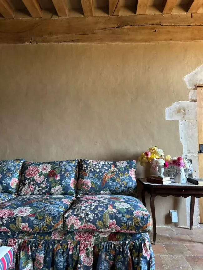 Floral-patterned sofa in a room with a textured wall and wooden beams.