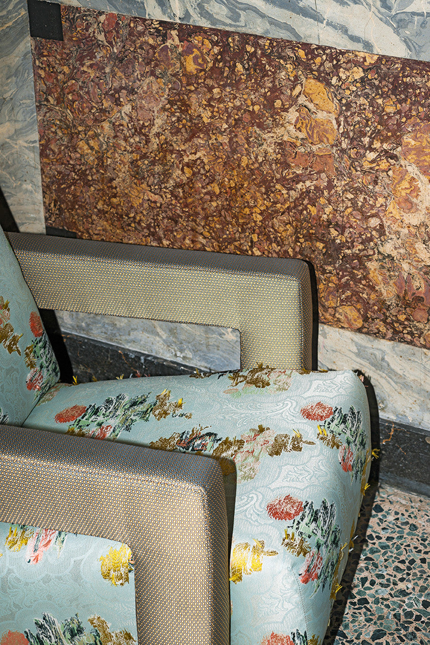 An image of a piece of fabric with yellow, blue and pink colours on a blue lace background, used as upholstery for a chair, available  to buy on the-salon.com. SALON curates the finest , unique, handmade pieces from the interior industry's best makers and brands. Shop luxury furniture, lighting, rugs, art, antiques and vintage pieces and accessories from SALON interior designed rooms.