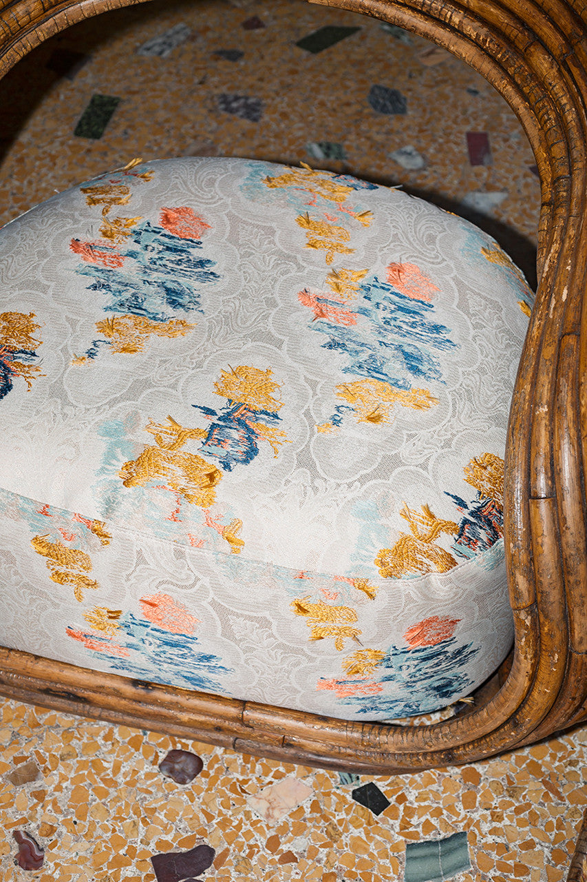 An image of a piece of fabric with yellow, blue and pink colours on a white lace background being used as upholstery , available  to buy on the-salon.com. SALON curates the finest , unique, handmade pieces from the interior industry's best makers and brands. Shop luxury furniture, lighting, rugs, art, antiques and vintage pieces and accessories from SALON interior designed rooms.