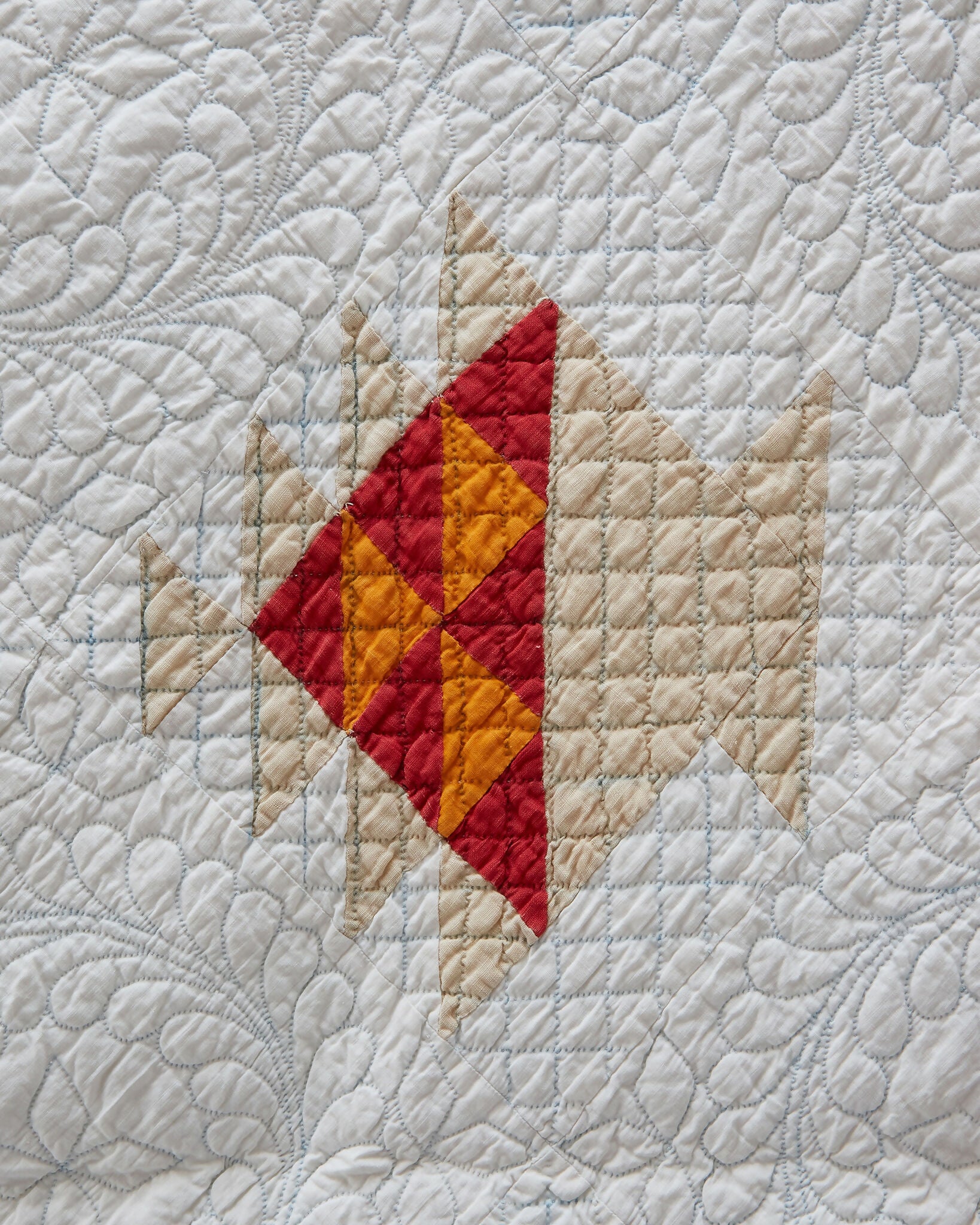 Close-up of a quilt with red and yellow triangle design on a white background,  available  to buy on the-salon.com. SALON curates the finest , unique, handmade pieces from the interior industry's best makers and brands. Shop luxury furniture, lighting, rugs, art, antiques and vintage pieces and accessories from SALON interior designed rooms.