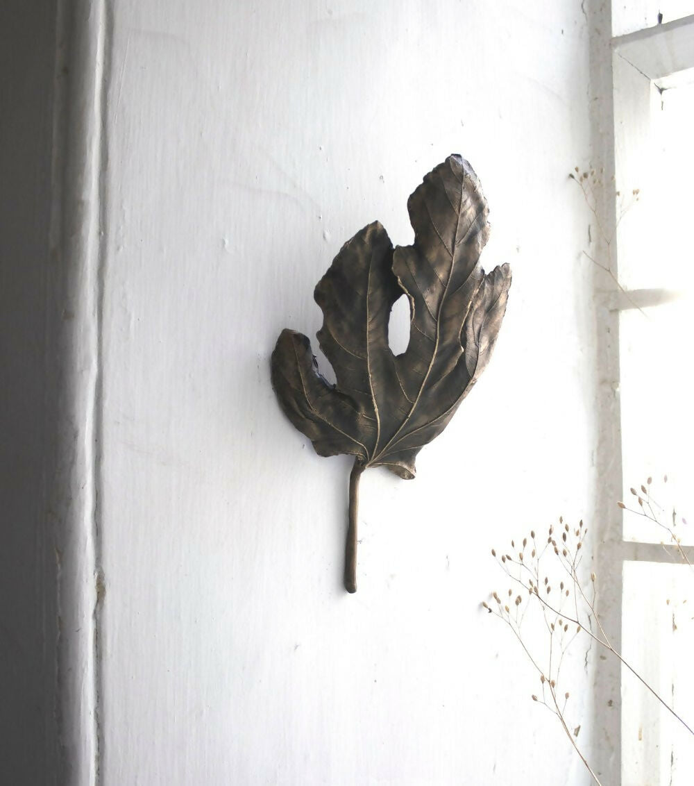 A bronze wall light fixture designed to resemble a fig leaf, with a textured surface and a wall mounting bracket,  available  to buy on the-salon.com. SALON curates the finest , unique, handmade pieces from the interior industry's best makers and brands. Shop luxury furniture, lighting, rugs, art, antiques and vintage pieces and accessories from SALON interior designed rooms.