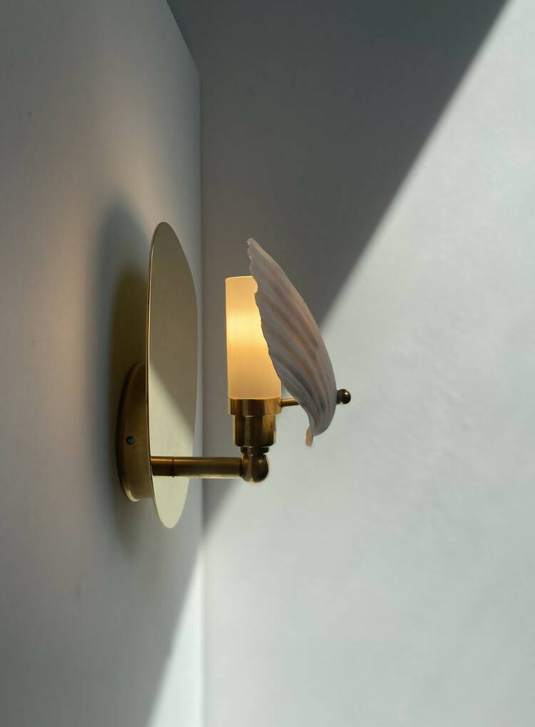 A wall light fixture with a chalky white scallop shell finish mounted on a polished brass backplate,  available  to buy on the-salon.com. SALON curates the finest , unique, handmade pieces from the interior industry's best makers and brands. Shop luxury furniture, lighting, rugs, art, antiques and vintage pieces and accessories from SALON interior designed rooms.