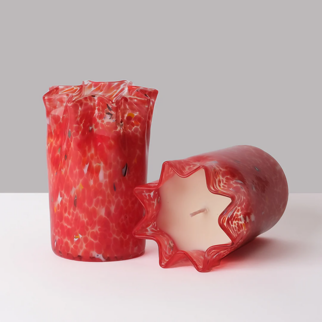 A custom hand-blown red glass candle with a geometric pattern, containing a scented wax and a wick, displayed on a white surface,  available  to buy on the-salon.com. SALON curates the finest , unique, handmade pieces from the interior industry's best makers and brands. Shop luxury furniture, lighting, rugs, art, antiques and vintage pieces and accessories from SALON interior designed rooms.