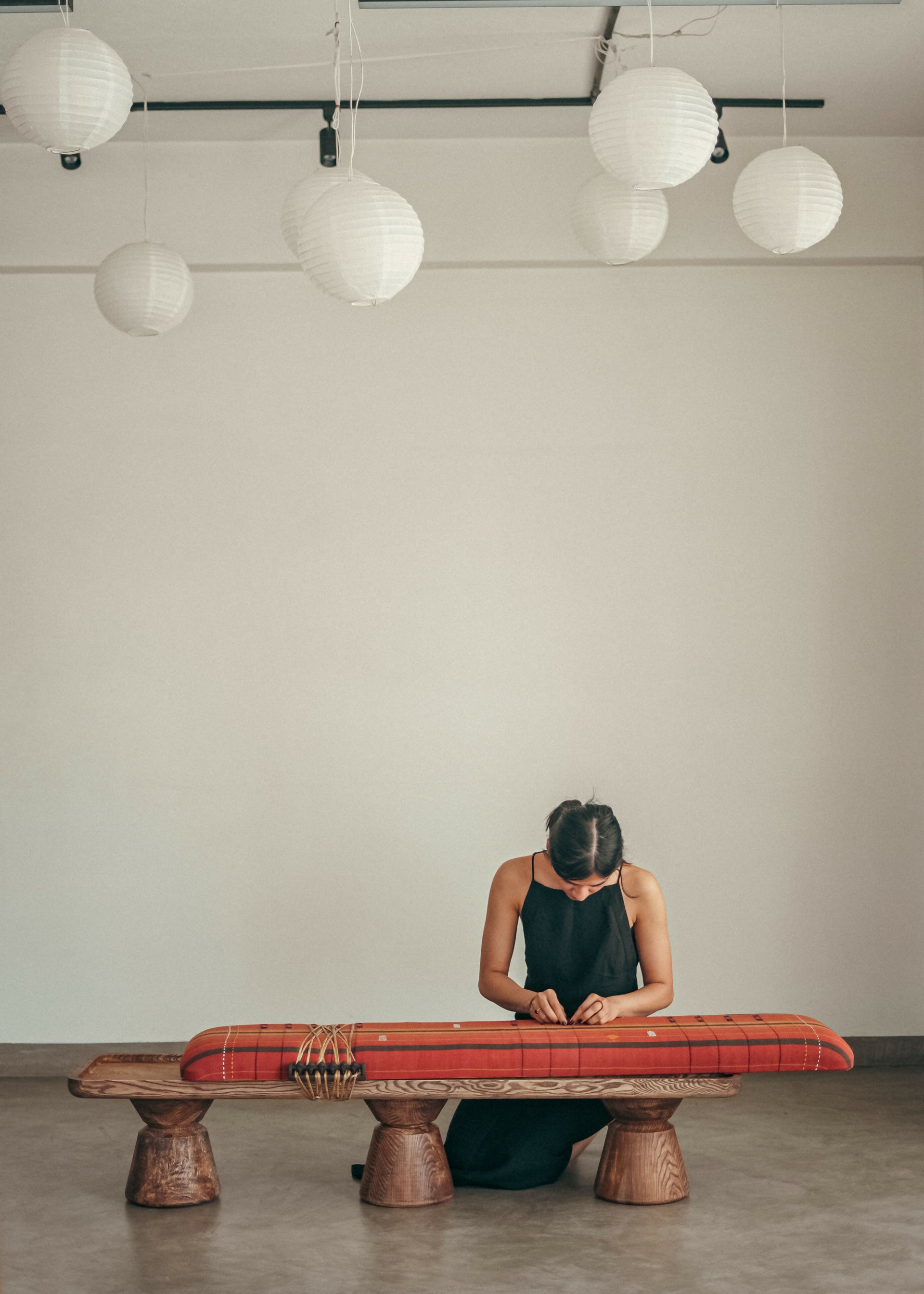 Person playing a traditional stringed instrument on a wooden bench in a minimalistic room,  available  to buy on the-salon.com. SALON curates the finest , unique, handmade pieces from the interior industry's best makers and brands. Shop luxury furniture, lighting, rugs, art, antiques and vintage pieces and accessories from SALON interior designed rooms.