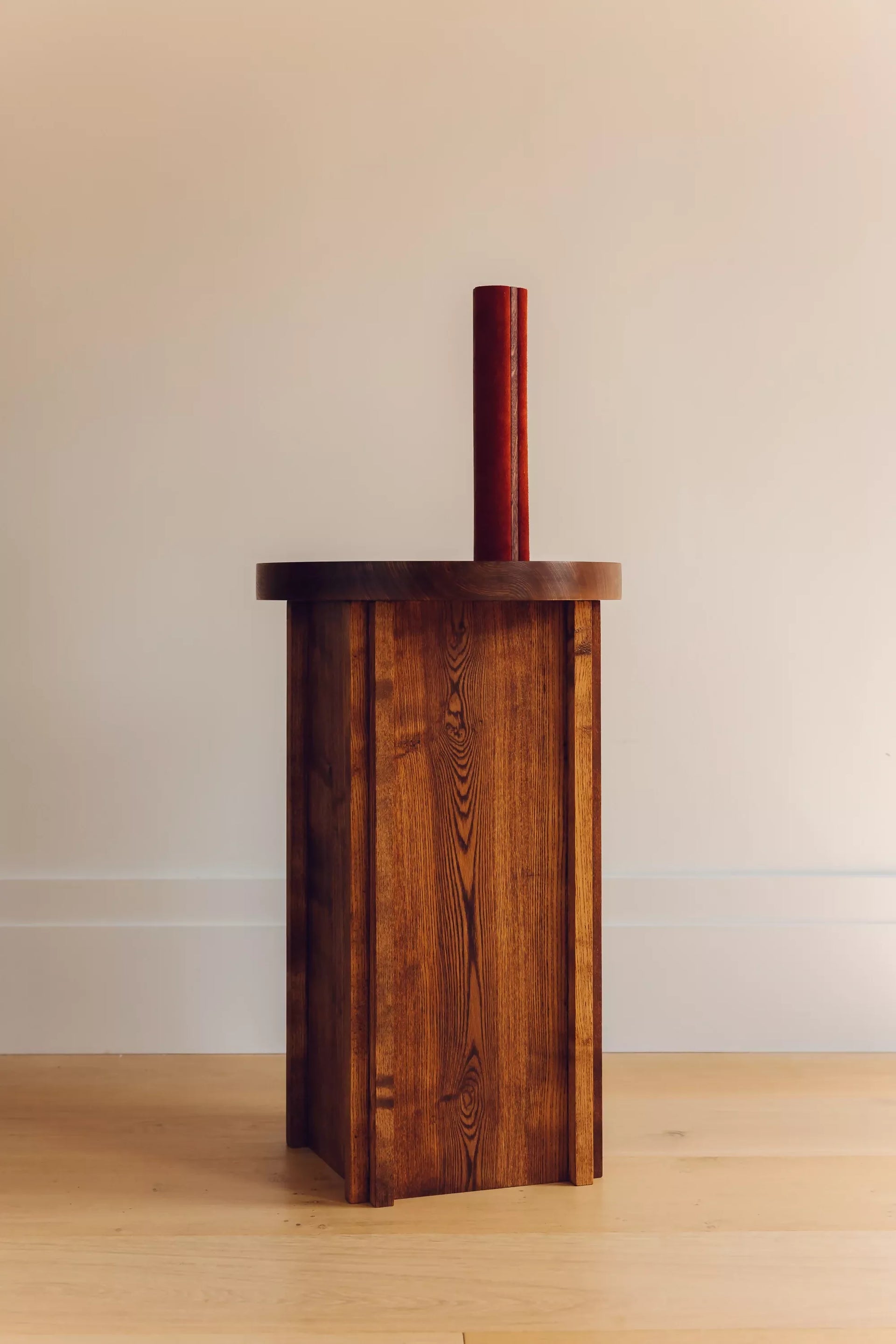 A view of the wooden side table in use, against a plain background , with a red candle ontop,  available  to buy on the-salon.com. SALON curates the finest , unique, handmade pieces from the interior industry's best makers and brands. Shop luxury furniture, lighting, rugs, art, antiques and vintage pieces and accessories from SALON interior designed rooms.