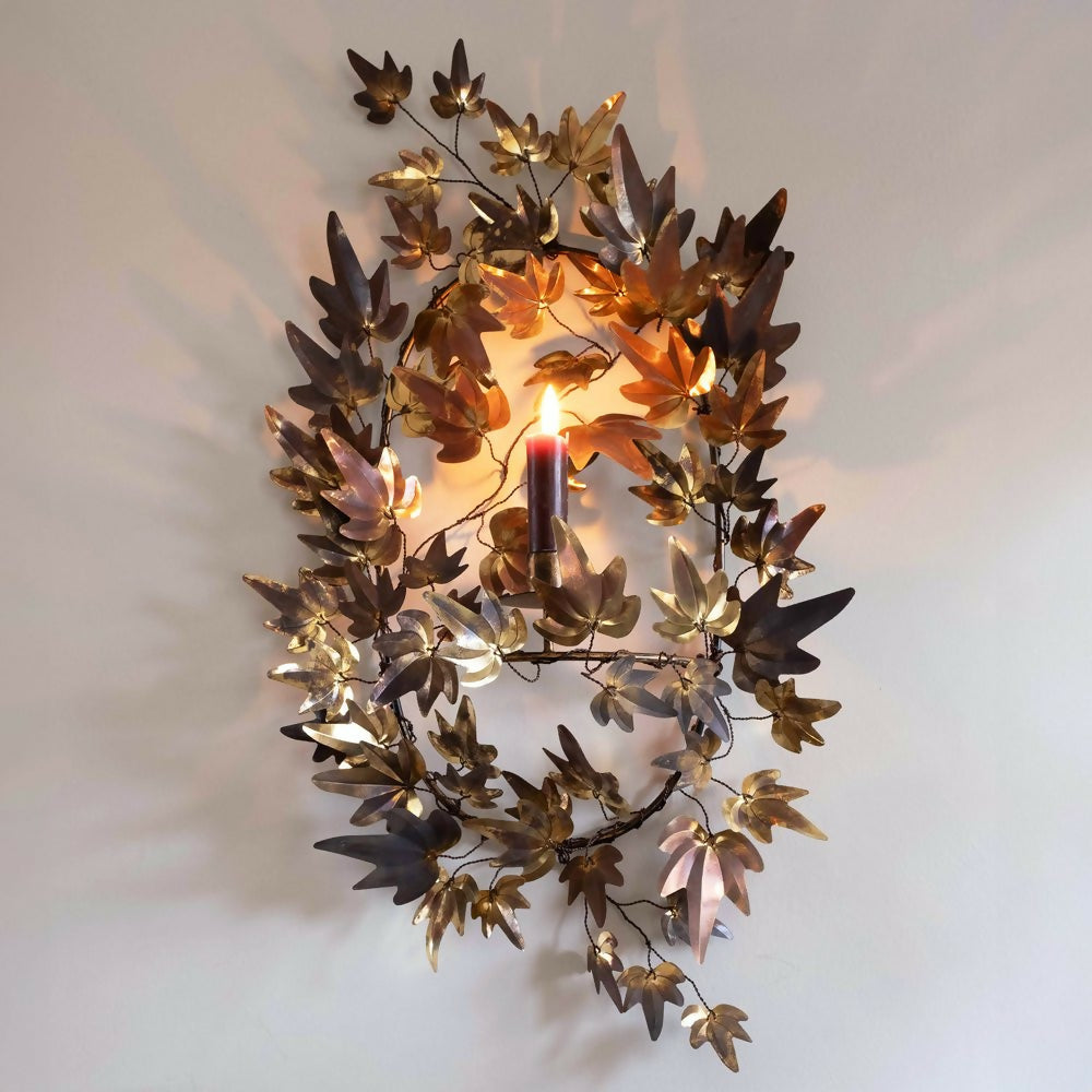 A brass candle wall sconce with patina finish designed by Jess Wheeler, featuring leaf shapes around a lit candle,   available  to buy on the-salon.com. SALON curates the finest , unique, handmade pieces from the interior industry's best makers and brands. Shop luxury furniture, lighting, rugs, art, antiques and vintage pieces and accessories from SALON interior designed rooms.