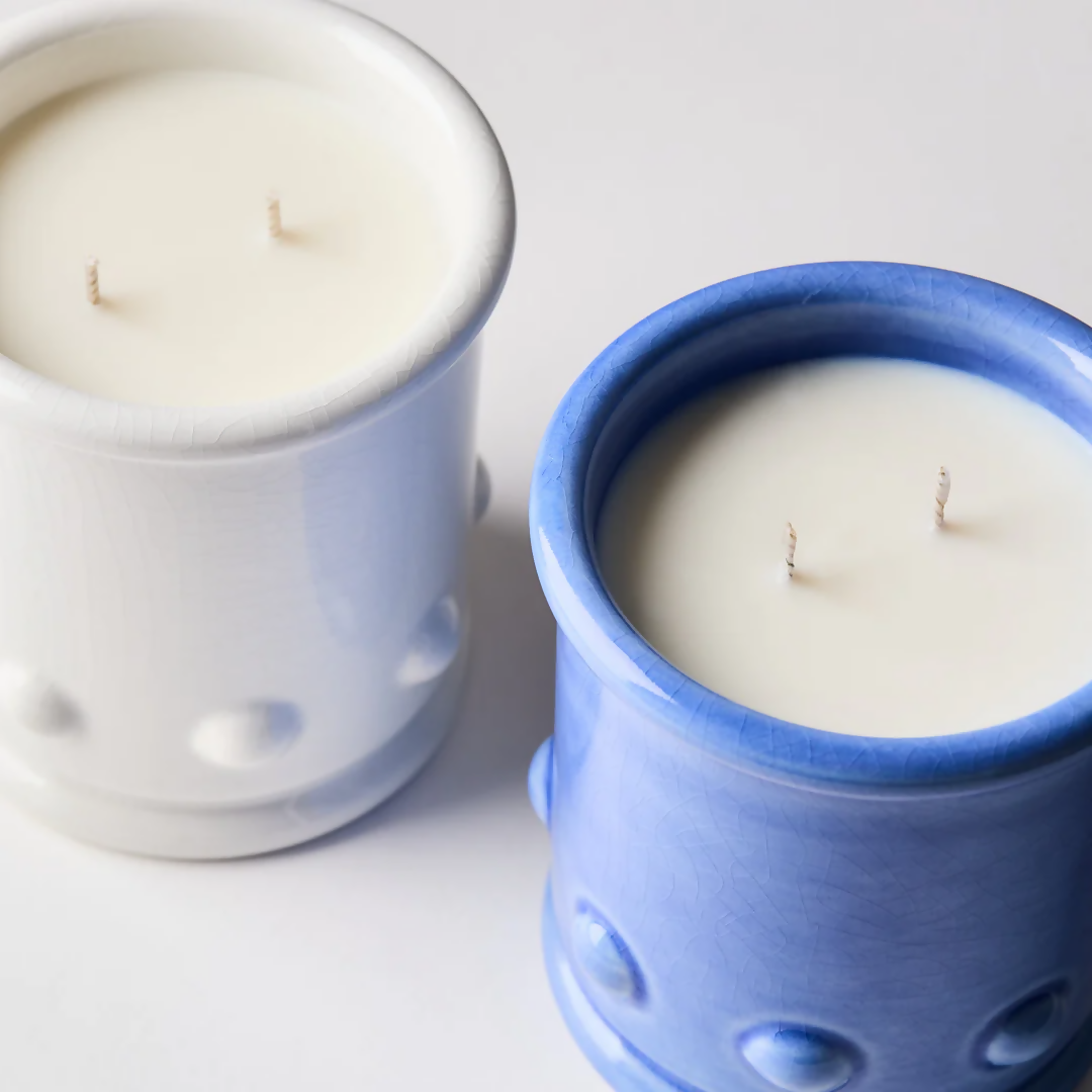 Blue and white ceramic candle vessels with spherical detailing on the sides, with a candle visible at the top. The vessel is placed against a neutral background,  available  to buy on the-salon.com. SALON curates the finest , unique, handmade pieces from the interior industry's best makers and brands. Shop luxury furniture, lighting, rugs, art, antiques and vintage pieces and accessories from SALON interior designed rooms.