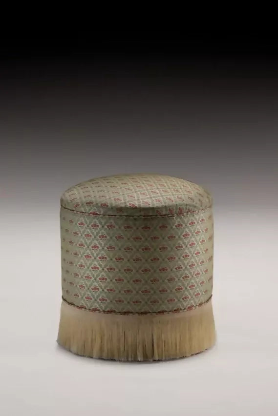 A textile fabric with a jacquard weave pattern featuring vibrant red poppies in a scallop shell vase, surrounded by foliage arranged in a trellis style, displayed on an ottoman,  available  to buy on the-salon.com. SALON curates the finest , unique, handmade pieces from the interior industry's best makers and brands. Shop luxury furniture, lighting, rugs, art, antiques and vintage pieces and accessories from SALON interior designed rooms.