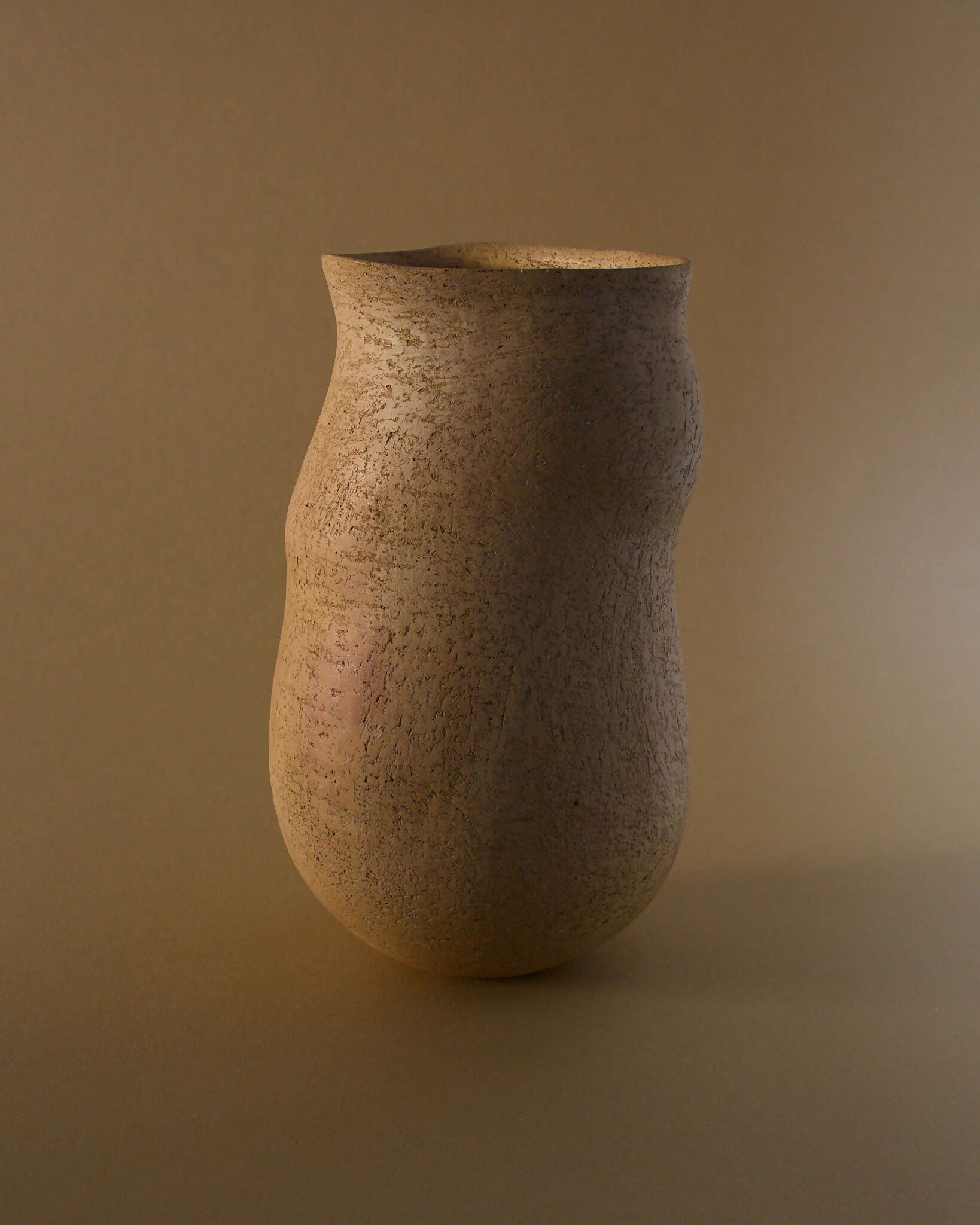 A brown ceramic vase with an organic, irregular silhouette, featuring a smooth yet textured surface with subtle flashes of burnt orange,  available  to buy on the-salon.com. SALON curates the finest , unique, handmade pieces from the interior industry's best makers and brands. Shop luxury furniture, lighting, rugs, art, antiques and vintage pieces and accessories from SALON interior designed rooms.