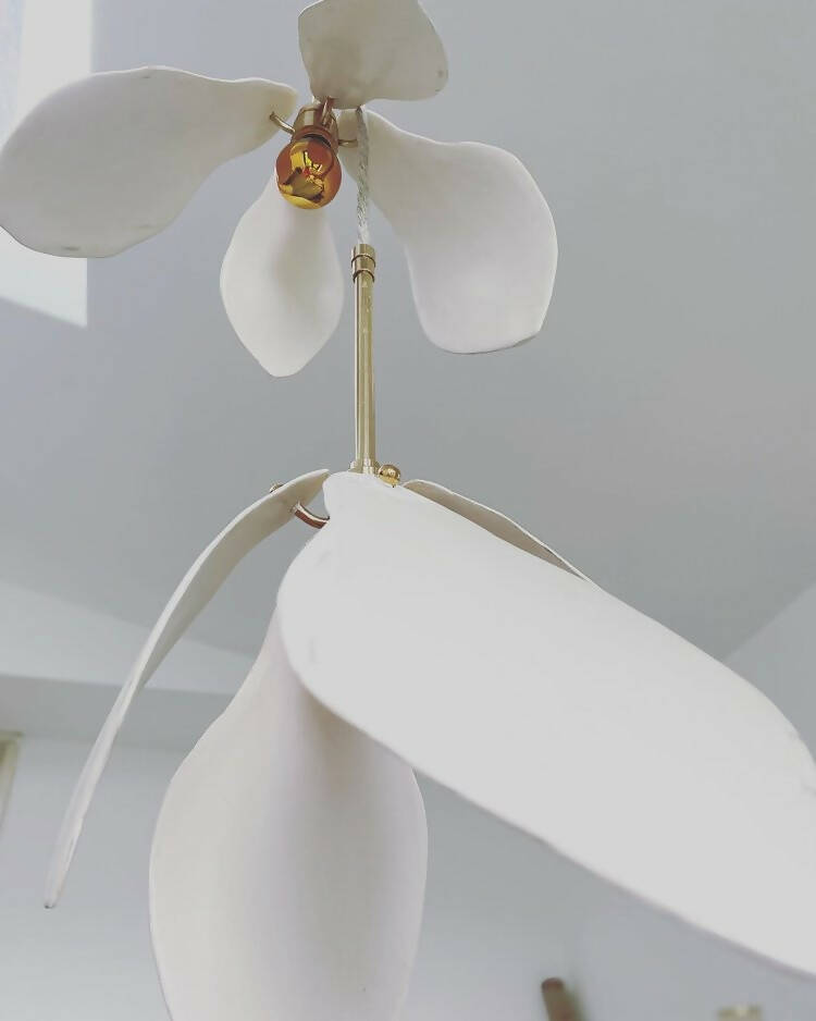 A close-up image of a white magnolia flower pendant light with a brass fitting and a gold-topped SES lamp,  available  to buy on the-salon.com. SALON curates the finest , unique, handmade pieces from the interior industry's best makers and brands. Shop luxury furniture, lighting, rugs, art, antiques and vintage pieces and accessories from SALON interior designed rooms.