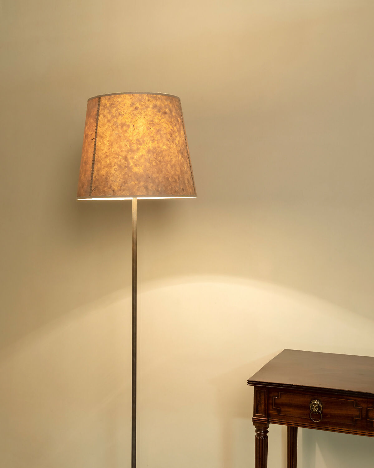 A beige hand stitched tapered lampshade made of Lokta paper with a natural linen trim, displayed on a lamp stand against a white background,  available  to buy on the-salon.com. SALON curates the finest , unique, handmade pieces from the interior industry's best makers and brands. Shop luxury furniture, lighting, rugs, art, antiques and vintage pieces and accessories from SALON interior designed rooms.
