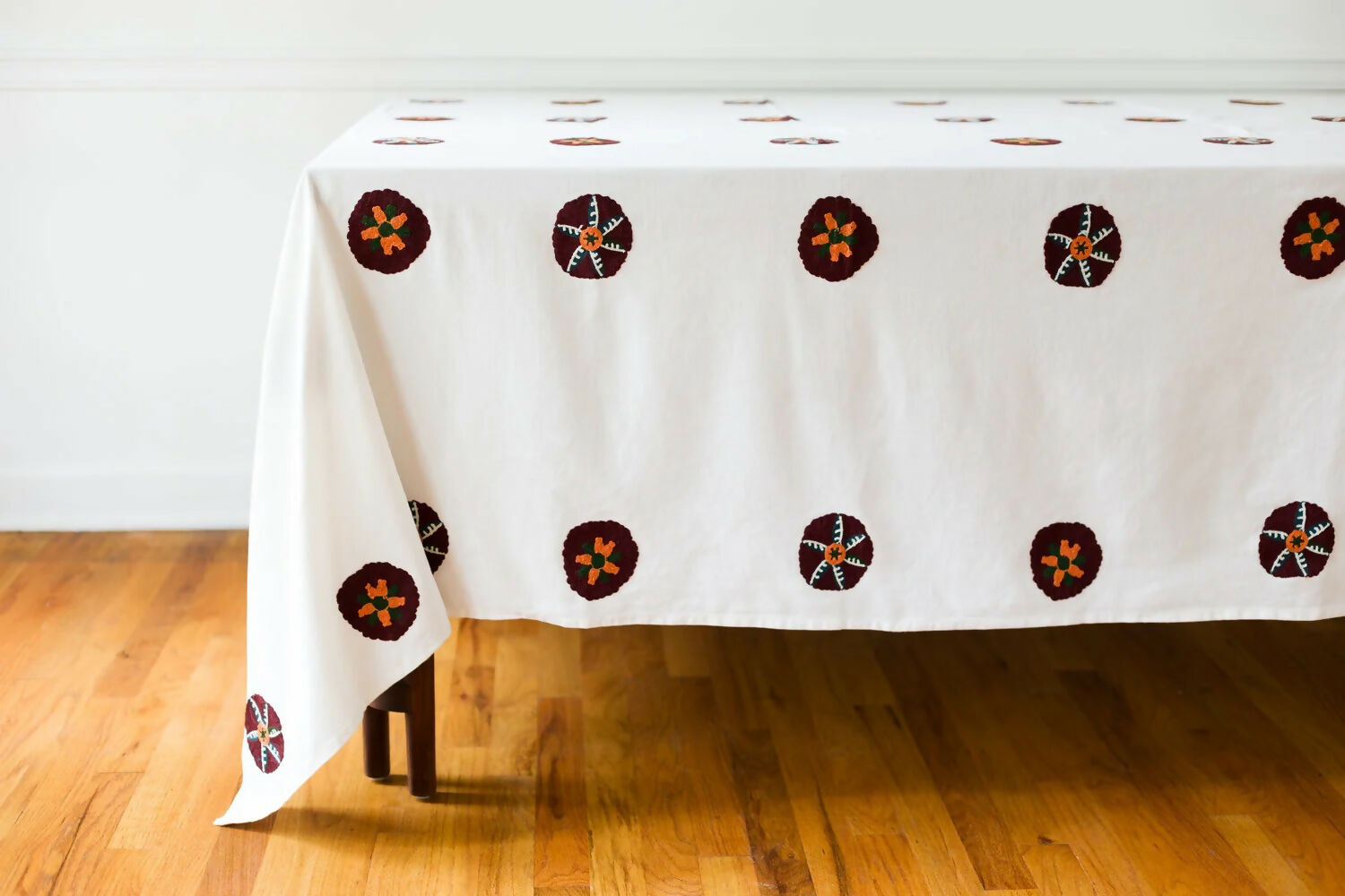 White tablecloth with brown circular patterns on a wooden floor,  available  to buy on the-salon.com. SALON curates the finest , unique, handmade pieces from the interior industry's best makers and brands. Shop luxury furniture, lighting, rugs, art, antiques and vintage pieces and accessories from SALON interior designed rooms.