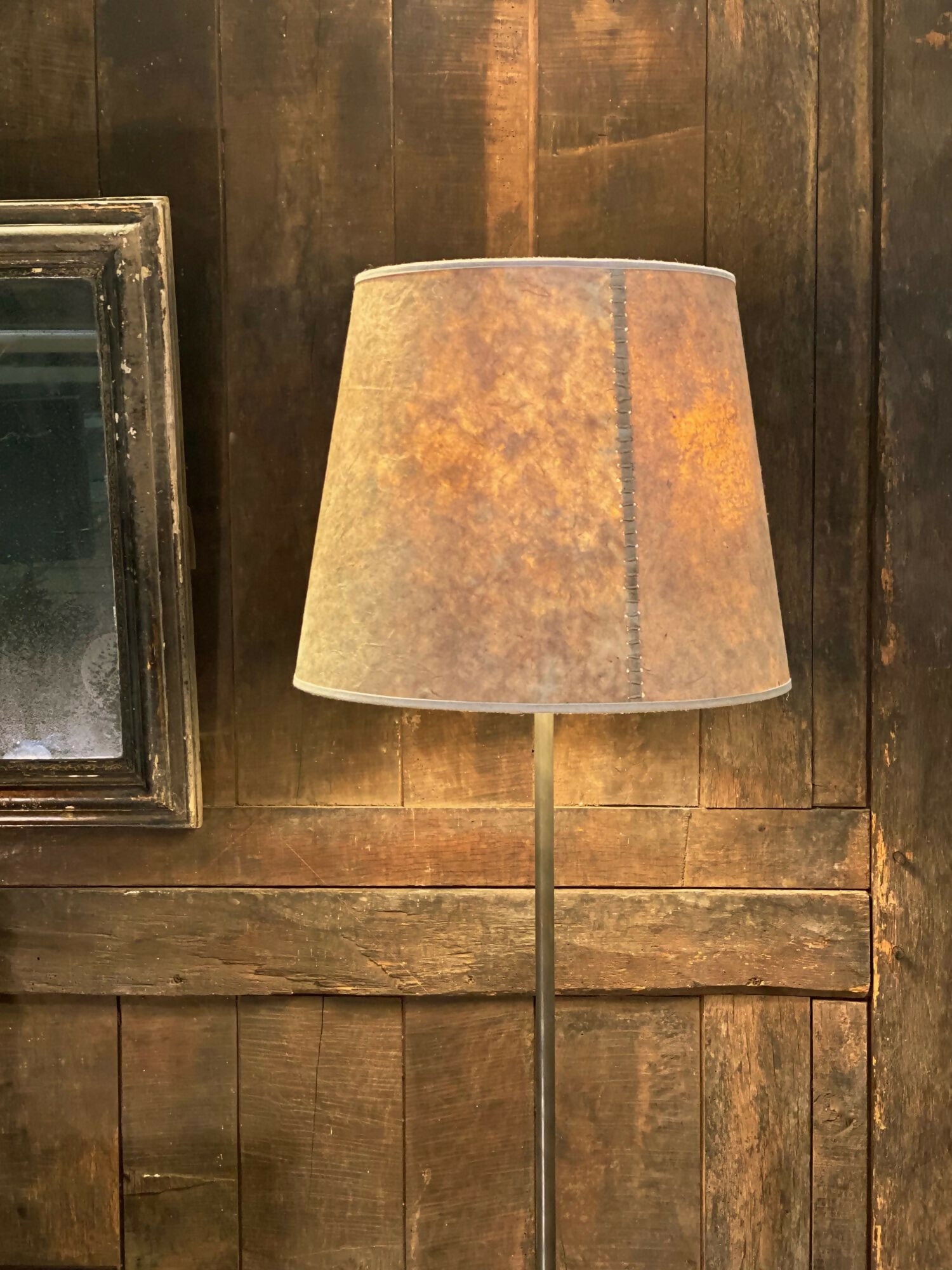 A beige hand stitched tapered lampshade made of Lokta paper with a natural linen trim, displayed on a lamp stand against a wooden background,  available  to buy on the-salon.com. SALON curates the finest , unique, handmade pieces from the interior industry's best makers and brands. Shop luxury furniture, lighting, rugs, art, antiques and vintage pieces and accessories from SALON interior designed rooms.