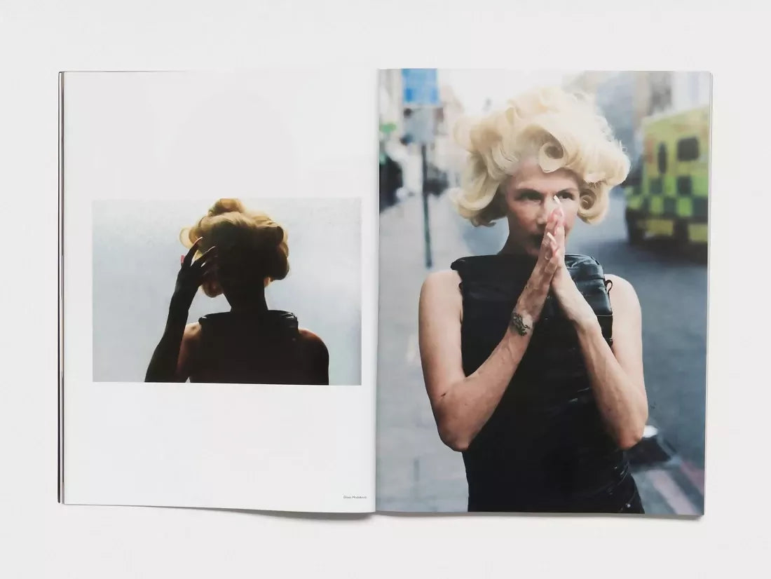 Open book, pages turned to an older woman with blonde, curled, styled hair on both sides, one where she is in darkness , the other with her hands covering her mouth in a prayer shape in a street with an ambulance behind her, available  to buy on the-salon.com. SALON curates the finest , unique, handmade pieces from the interior industry's best makers and brands. Shop luxury furniture, lighting, rugs, art, antiques and vintage pieces and accessories from SALON interior designed rooms. 