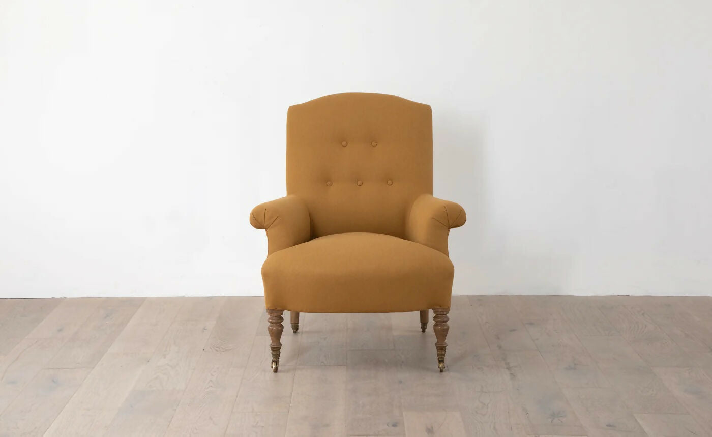A brown upholstered armchair with button back detailing and scroll arms, set against a white background,  available  to buy on the-salon.com. SALON curates the finest , unique, handmade pieces from the interior industry's best makers and brands. Shop luxury furniture, lighting, rugs, art, antiques and vintage pieces and accessories from SALON interior designed rooms.