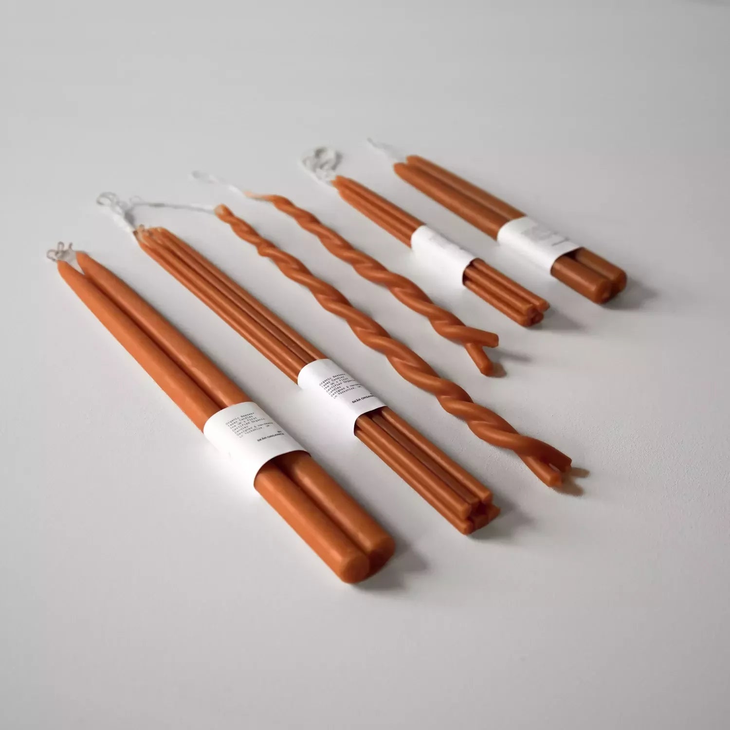 A selection of hand-dipped beeswax dinner candles in paprika color, hanging on a rack, with packaging around the base,  available  to buy on the-salon.com. SALON curates the finest , unique, handmade pieces from the interior industry's best makers and brands. Shop luxury furniture, lighting, rugs, art, antiques and vintage pieces and accessories from SALON interior designed rooms.
