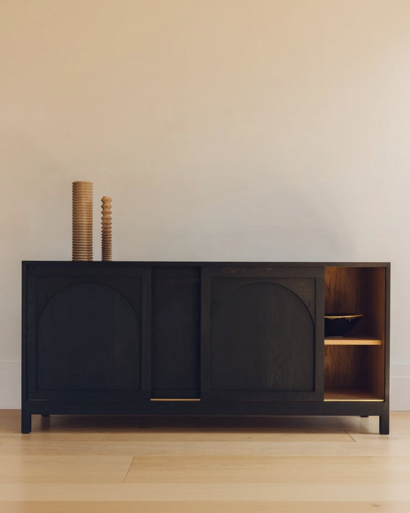 Dark wooden sideboard with arched doors in a minimalistic room.
