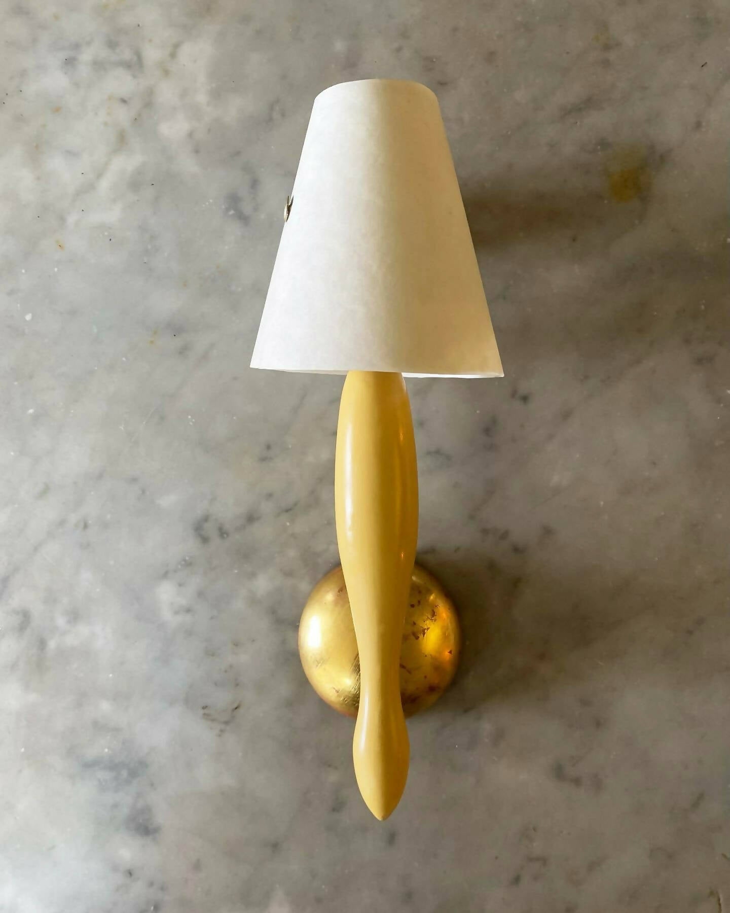 A yellow wall light with white on a marble grey background. SALON curates the finest unique handmade pieces from the interior industry's best makers and brands. Shop luxury furniture, lighting, rugs, art, antiques and vintage pieces and accessories from SALON interior designed rooms.
