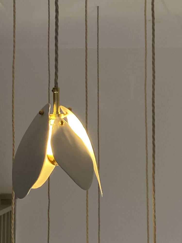A close-up image of a white magnolia flower pendant light with a brass fitting and a gold-topped SES lamp,  available  to buy on the-salon.com. SALON curates the finest , unique, handmade pieces from the interior industry's best makers and brands. Shop luxury furniture, lighting, rugs, art, antiques and vintage pieces and accessories from SALON interior designed rooms.