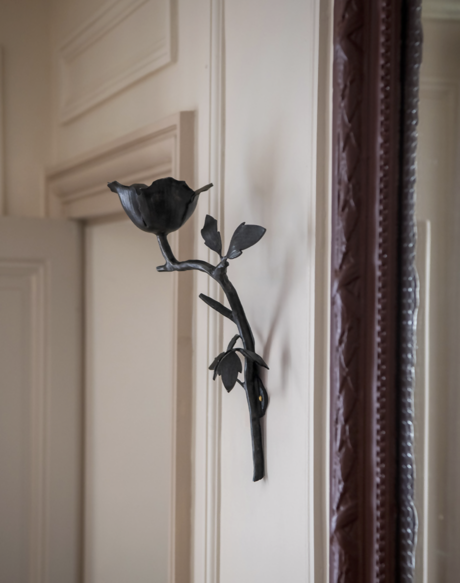 A wall-mounted black iron candle sconce in the shape of a clematis flower,  available  to buy on the-salon.com. SALON curates the finest , unique, handmade pieces from the interior industry's best makers and brands. Shop luxury furniture, lighting, rugs, art, antiques and vintage pieces and accessories from SALON interior designed rooms.