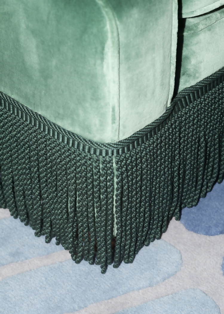 A green velvet sofa with plush seats and a tasseled fringe, named 'Large Atlanta Sofa by Orior', With a close up on the tasseled fringe, available  to buy on the-salon.com. SALON curates the finest , unique, handmade pieces from the interior industry's best makers and brands. Shop luxury furniture, lighting, rugs, art, antiques and vintage pieces and accessories from SALON interior designed rooms.