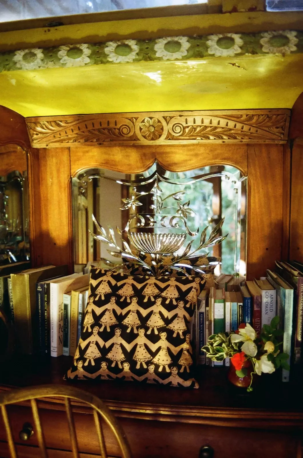 A square-shaped cushion with a geometric pattern, featuring black and gold colors, displayed in front of a dresser with an ornate wooden frame,  available  to buy on the-salon.com. SALON curates the finest , unique, handmade pieces from the interior industry's best makers and brands. Shop luxury furniture, lighting, rugs, art, antiques and vintage pieces and accessories from SALON interior designed rooms.